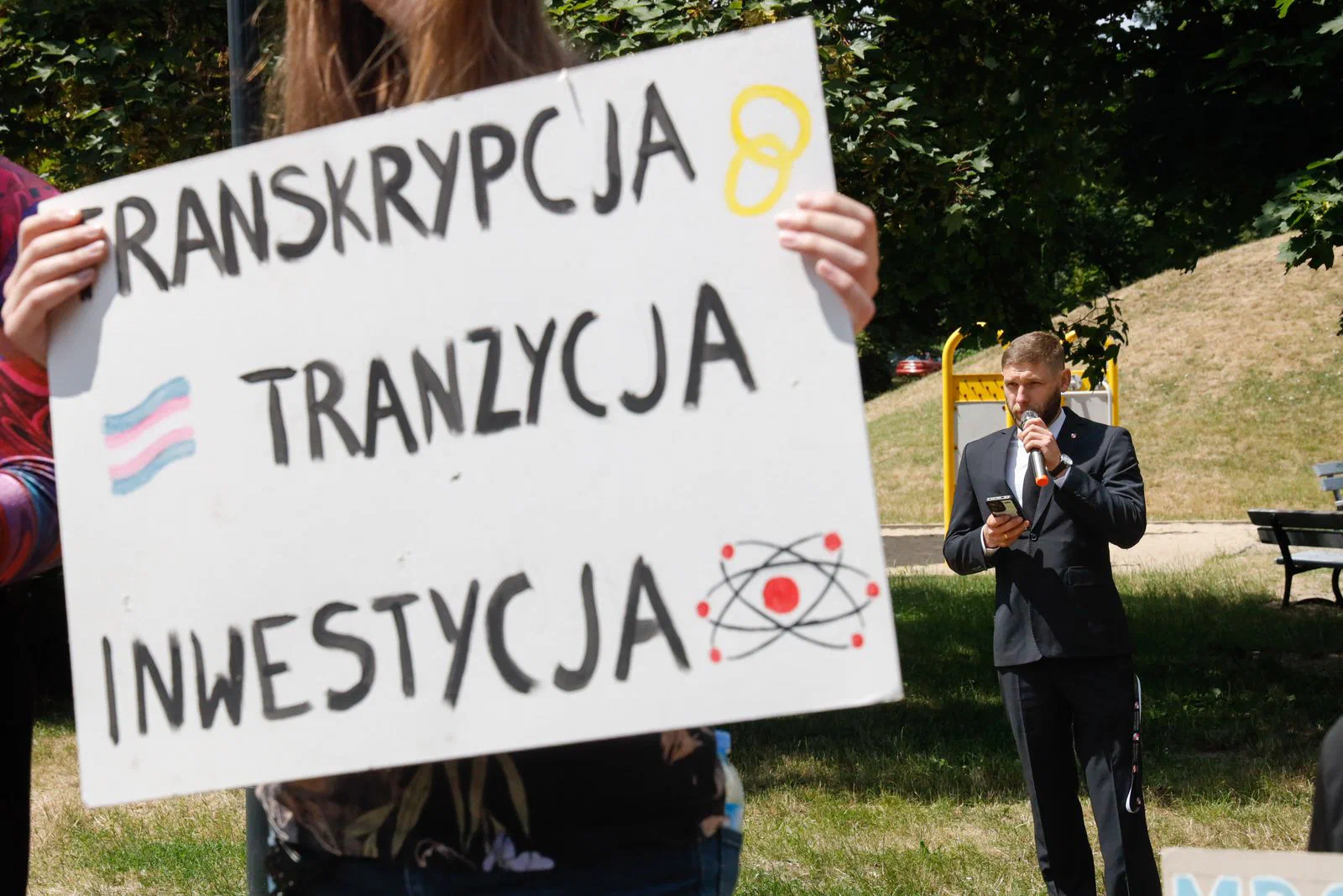 Osoba trzyma dużą tabliczkę z napisem Transkrypcja Tranzycja Inwestycja