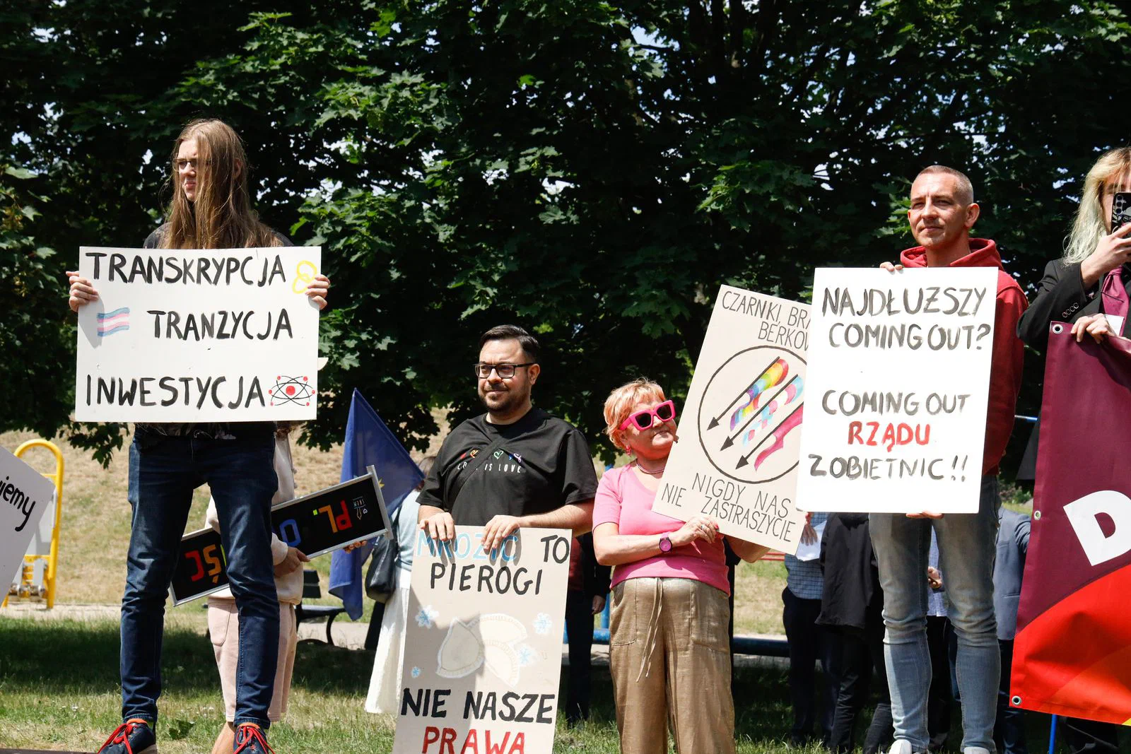Uczestnicy Pikniku Równości z transparentami i flagą Partii Razem w parku